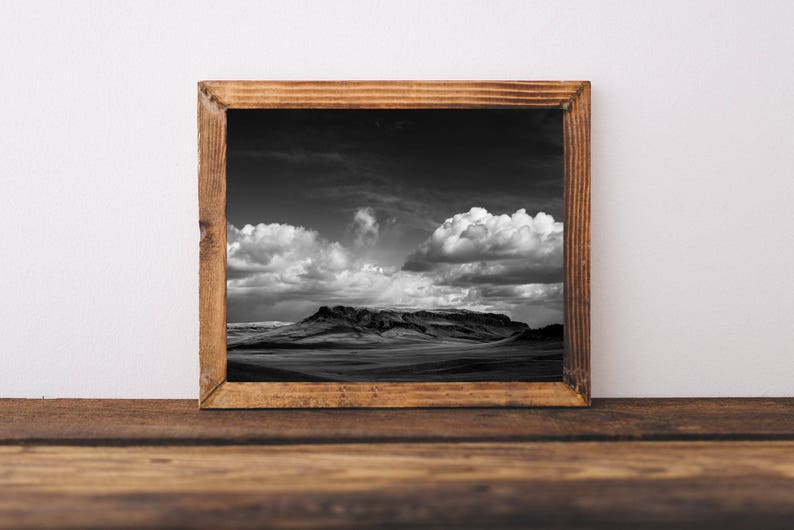 May include: A black and white photograph of a mountain range with a cloudy sky. The photo is framed in a rustic wooden frame.