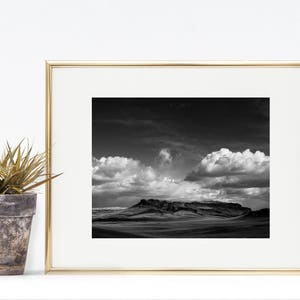 May include: A black and white photograph of a mountain range with a cloudy sky. The photo is framed in a gold frame.