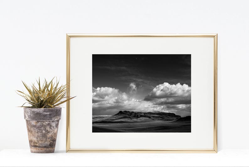 May include: A black and white photograph of a mountain range with a cloudy sky. The photo is framed in a gold frame.