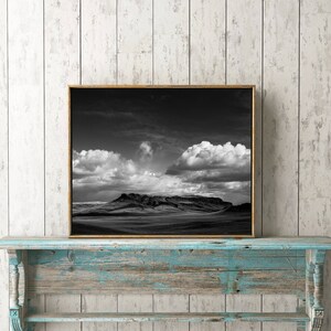 May include: A black and white photograph of a mountain range with clouds in the sky, framed in a gold frame and displayed on a blue and white distressed wooden shelf.