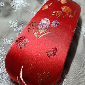 May include: Red satin eyeglass case with a floral pattern in gold, red, and purple.