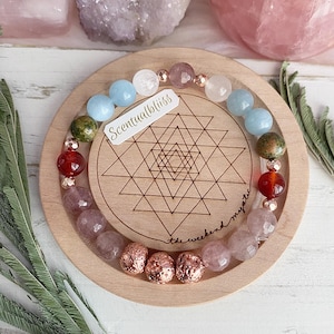 May include: A bracelet made with various semi-precious stones, including rose quartz, aquamarine, and carnelian. The bracelet is on a wooden display with a geometric pattern and the text "Scentualbliss the weekend mystic".