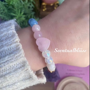 May include: A bracelet with pink heart-shaped and round beads, a blue bead, and iridescent and white beads. The text "Scentualbliiss" is visible on the wrist. The bracelet is a piece of jewellery.