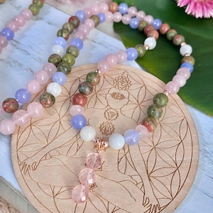 May include: A multi-strand mala necklace with pink, green and blue beads. The necklace has a rose gold pendant with a pink crystal drop.