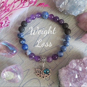 May include: A bracelet featuring amethyst, blue sodalite, and black lava beads. A silver lotus flower charm with a blue gem is attached. The image includes the text "Weight Loss".