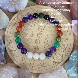 May include: A multi-coloured gemstone bracelet featuring purple, green, orange, and white beads. The bracelet is presented on a wooden coaster with engraved patterns and the text "Aromatherapy Diffuser".
