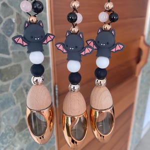 Può includere: Tre profumatori per auto sospesi a tema pipistrello. Ognuno ha un ciondolo a forma di pipistrello nero con ali rosa, perline bianche e nere e una bottiglia di vetro color oro rosa. La parte superiore di ogni profumatore ha perline nere e rosa.