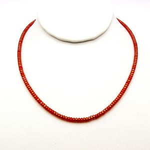 May include: A simple necklace made of small, orange-colored beads. The beads are iridescent and have a slight shimmer to them.