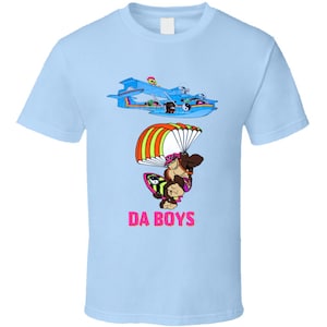 May include: Pale blue t-shirt with a cartoon graphic of a blue seaplane and a character with a parachute and surfboard. The text "DA BOYS" is printed in pink below the character.