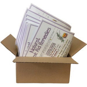 Puede incluir: Una caja de cartón con la tapa abierta, que revela una pila de hojas impresas con el título "Natural First Aid Remedies". Las hojas están impresas con un borde morado y presentan ilustraciones de hierbas y otros remedios naturales.