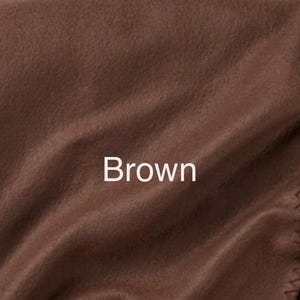 May include: A solid brown fleece blanket featuring a soft, matte texture with visible folds and a stitched edge detail. The word Brown is printed in white text in the centre of the fabric, indicating the colour of the material.