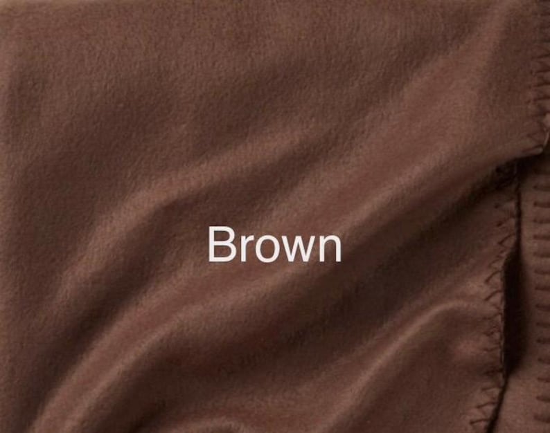 May include: A solid brown fleece blanket featuring a soft, matte texture with visible folds and a stitched edge detail. The word Brown is printed in white text in the centre of the fabric, indicating the colour of the material.
