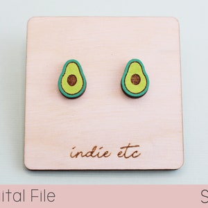 May include: Two avocado-shaped stud earrings with green, brown, and teal accents. The earrings are displayed on a light-colored wooden square with the text "indie etc" and the words "Digital File" and "SVG".