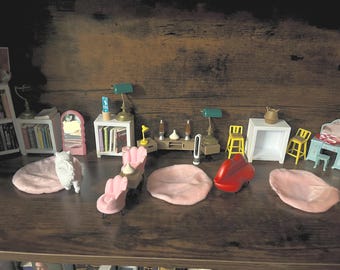 Könnte beinhalten: Miniatur-Puppenhausmöbel-Set, darunter rosa Stühle, ein rotes Sofa und ein blauer Schreibtisch. Das Set umfasst auch kleine Lampen, Bücherregale und einen Spiegel, alles auf einem Holzregal angeordnet. Das Thema ist ein gemütlicher, miniaturisierter Wohnraum.