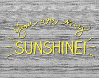 May include: Yellow text on a gray wood-grain background reads "You are my SUNSHINE!". The words are in a handwritten style, with the word "SUNSHINE!" in a bold font. The bottom left corner has the text "Flexible designs".