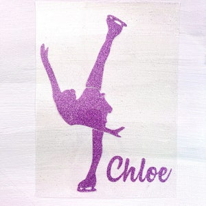 May include: A purple glitter vinyl decal featuring a figure skater in a dynamic pose. The skater is depicted mid-routine, with one leg extended and an arm raised. The name "Chloe" is written in cursive script below. The decal is set against a white backdrop.