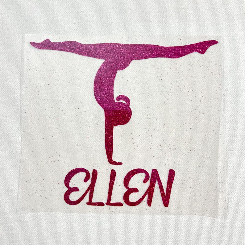 May include: A pink glitter decal featuring a silhouette of a gymnast performing a handstand with the name ELLEN printed in a bold, cursive font underneath the figure. The design is presented on a clear, adhesive backing material.