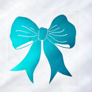 May include: A vibrant metallic teal bow graphic printed on a white fabric surface. The design features a central knot with two large loops and two downward-pointing ribbon tails, showcasing a smooth, reflective finish with subtle gradient shading.