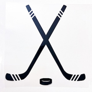 May include: Black graphic of two crossed hockey sticks with white stripes and a hockey puck on a white background. The hockey sticks are angled in an X shape, and the puck is a small black circle.