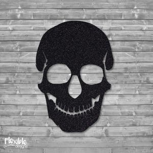 May include: A black skull silhouette with a textured surface. The skull has large eye sockets, a prominent nose cavity, and a detailed jawline. The design is set against a gray wooden plank background. The text "Flexible designs" is in the bottom left corner.
