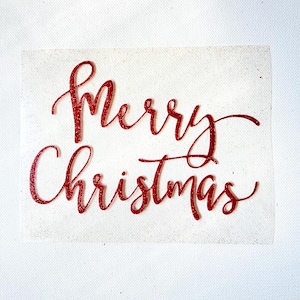 May include: A rectangular white fabric patch featuring the red glittery text Merry Christmas in a cursive script font. The lettering is centred on the fabric, which has a subtle speckled texture throughout its surface.