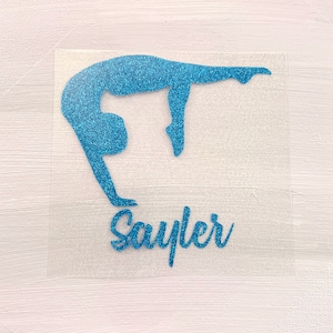 Puede incluir: Silueta de gimnasta azul brillante en posición de pino. El nombre "Sayler" está escrito en cursiva debajo. La imagen está sobre un fondo transparente y cuadrado.