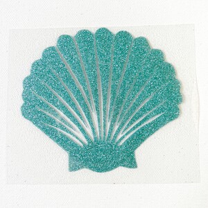May include: A teal glitter seashell design on a clear background. The seashell has a fan-like shape with detailed lines radiating from the centre. The glitter adds a sparkling effect, making it visually appealing. This design is suitable for crafts and coastal-themed projects.