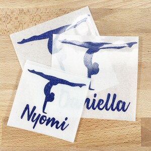 May include: Three square adhesive decals featuring a dark blue glitter gymnast silhouette in a handstand position. Two of the decals include the names Nyomi and Daniella printed in a dark blue glitter script font below the gymnast figure.