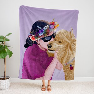 K&ouml;nnte beinhalten: Eine lilafarbene Fleece-Decke mit einer Aquarell-Illustration einer Person, die eine Blumenkrone und eine Sonnenbrille tr&auml;gt und einen Goldendoodle-Hund k&uuml;sst.