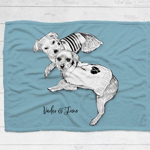 Puede incluir: Una manta de franela azul claro con una ilustraci&oacute;n en blanco y negro de dos perros con su&eacute;teres. El texto "Vader & Juno" est&aacute; impreso en la manta.