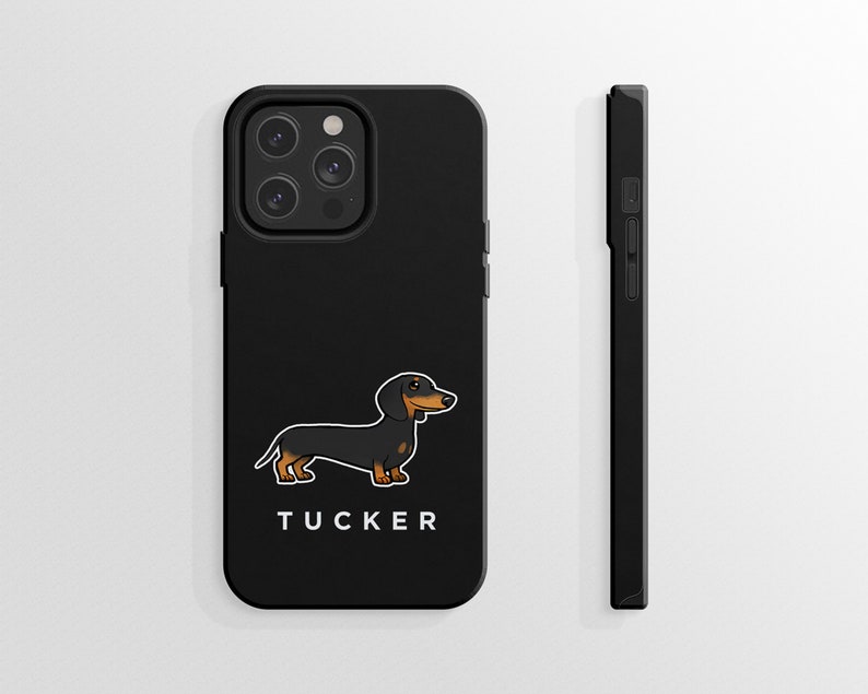 K&ouml;nnte beinhalten: Schwarze Handyh&uuml;lle mit einem Cartoon-Dackel und dem Namen "TUCKER" darauf.