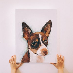 Puede incluir: Una pintura de acuarela de un perro marr&oacute;n y blanco con la nariz negra. El perro tiene ojos grandes y oscuros y mira directamente al espectador.