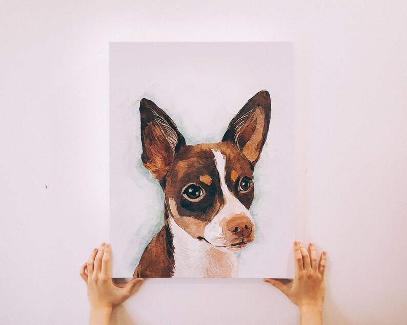 Puede incluir: Una pintura de acuarela de un perro marr&oacute;n y blanco con la nariz negra. El perro tiene ojos grandes y oscuros y mira directamente al espectador.