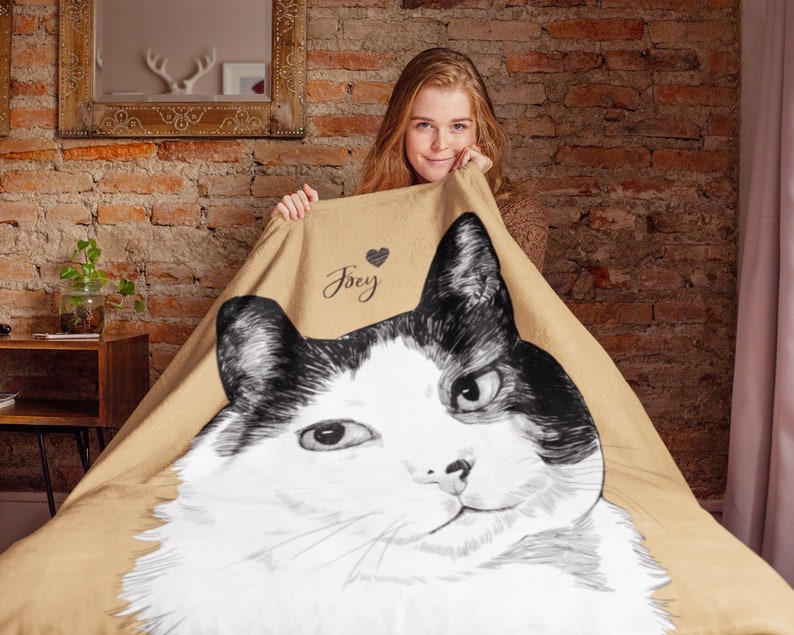 Puede incluir: Una manta de forro polar de color beige con una ilustraci&oacute;n en blanco y negro de un gato. El nombre del gato, "Joey", est&aacute; escrito en la manta con un coraz&oacute;n.