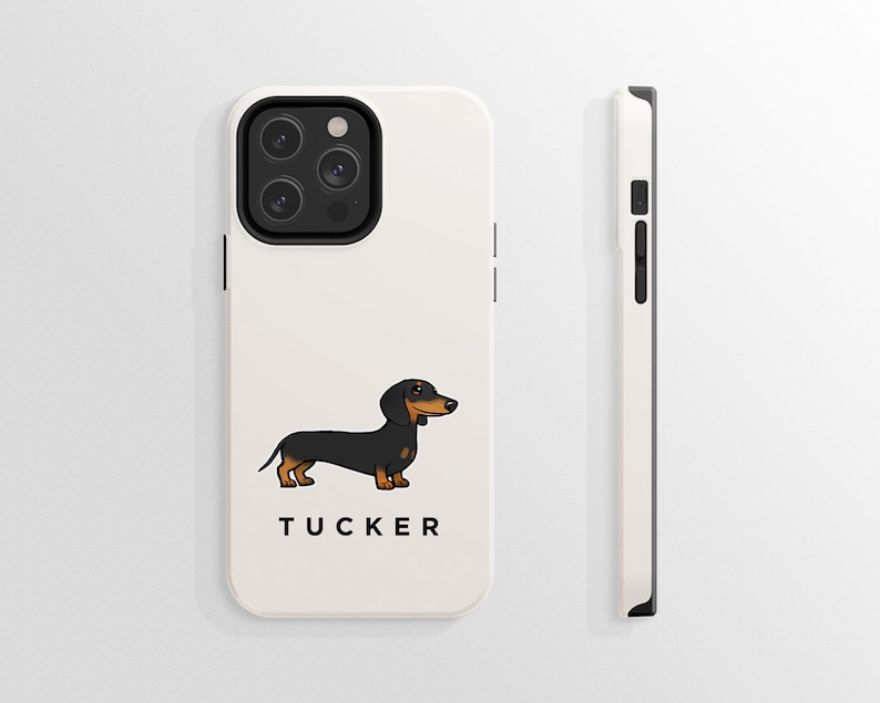 K&ouml;nnte beinhalten: Wei&szlig;e iPhone-H&uuml;lle mit einer Cartoon-Illustration eines schwarzen und braunen Dackels und dem Namen "TUCKER" darunter. Die H&uuml;lle hat eine schwarze Kamera-Erhebung mit drei Objektiven.