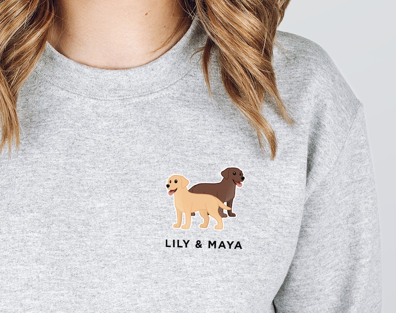Pode incluir: Uma camisa de moletom cinza com uma imagem de desenho animado de dois labradores, um marrom e um amarelo, com o texto "LILY & MAYA" abaixo da imagem.