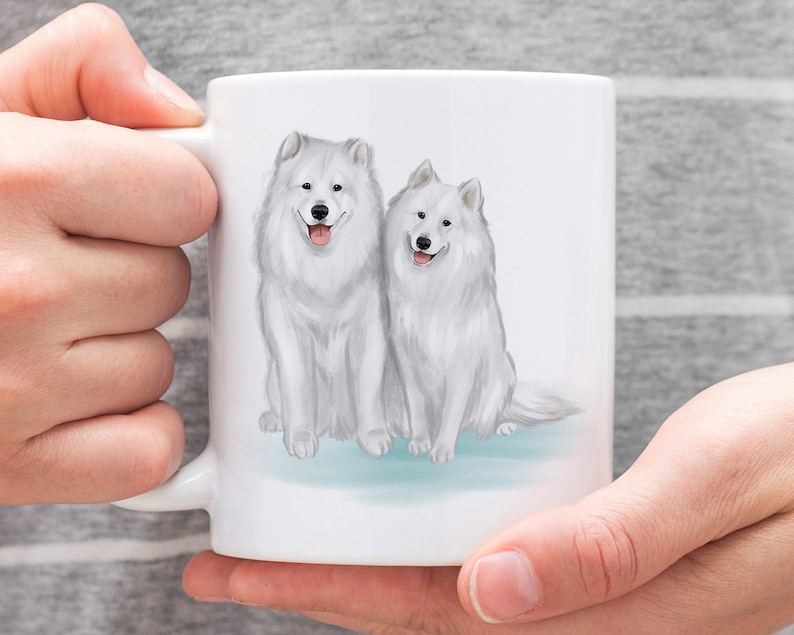 K&ouml;nnte beinhalten: Wei&szlig;e Keramiktasse mit einer Aquarell-Illustration von zwei wei&szlig;en Samojeden, die nebeneinander sitzen.