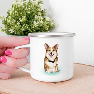 K&ouml;nnte beinhalten: Wei&szlig;e Emaille-Campingtasse mit einem braunen und wei&szlig;en Corgi, der eine schwarze Fliege tr&auml;gt. Der Corgi sitzt auf einem hellblauen Hintergrund.