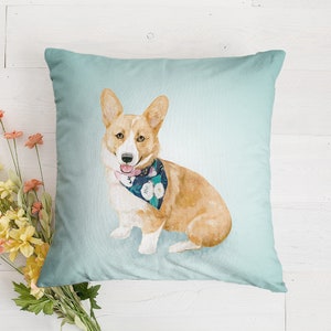 May include: A light blue throw pillow with a watercolor illustration of a corgi wearing a floral bandana. The corgi is looking to the right and has a pink tongue sticking out.