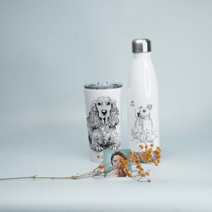 May include: White stainless steel water bottle and tumbler with black and white illustrations of dogs. The water bottle has the word "Lola" printed on it. The tumbler has a small photo of a person on the bottom.