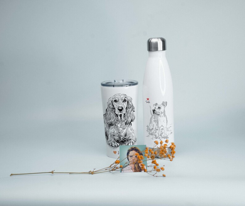 May include: White stainless steel water bottle and tumbler with black and white illustrations of dogs. The water bottle has the word "Lola" printed on it. The tumbler has a small photo of a person on the bottom.