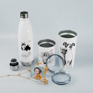 May include: Three white stainless steel tumblers with lids. The tumblers feature black and white illustrations of dogs and a deer. One tumbler has the name "Oliver" on it. The tumblers are on a white surface with a small bouquet of yellow flowers.
