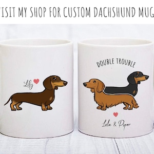 Puede incluir: Dos tazas de cer&aacute;mica blanca con ilustraciones de dachshund. Una taza presenta un dachshund marr&oacute;n con el nombre "Lily" y un coraz&oacute;n. La otra taza presenta un dachshund negro y marr&oacute;n con el texto "Double Trouble" y los nombres "Lala & Piper" con un coraz&oacute;n.