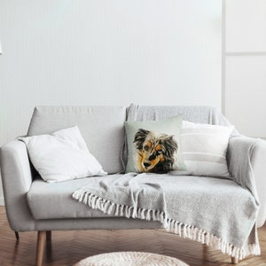 May include: A gray couch with a throw blanket and a pillow featuring a watercolor painting of a dog's face.