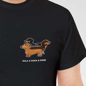 May include: Black t-shirt featuring a graphic of three dachshund dogs in brown, black, and tan. The text "NALA & KONA & PIPER" is printed below the dogs in white. The shirt is made of a soft material.