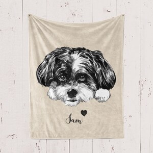 Puede incluir: Una manta de forro polar beige con una ilustraci&oacute;n en blanco y negro de la cara de un perro. El nombre del perro, "Sam", est&aacute; escrito en cursiva debajo de la imagen con un peque&ntilde;o coraz&oacute;n negro.
