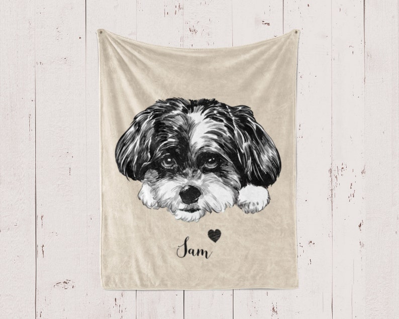 Puede incluir: Una manta de forro polar beige con una ilustraci&oacute;n en blanco y negro de la cara de un perro. El nombre del perro, "Sam", est&aacute; escrito en cursiva debajo de la imagen con un peque&ntilde;o coraz&oacute;n negro.