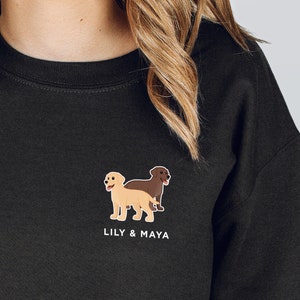 Pode incluir: Camisola de moletom preta com um gr&aacute;fico de dois labradores, um marrom claro e outro marrom escuro, com o texto "Lily & Maya" embaixo.