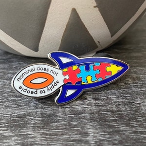 May include: A blue and white rocket pin with a puzzle piece design and the text "nominal does not add to doodle".