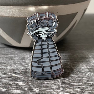 May include: A silver-colored rocket engine pin with a detailed design. The engine is depicted in a gray color with white accents. The pin is a great addition to any space enthusiast's collection.